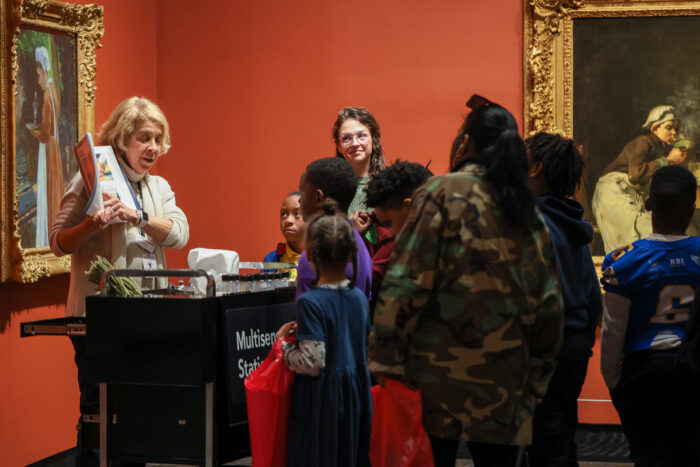 Docent holding up a book talking to a group of people in the gallery