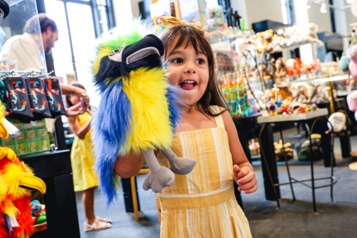 young girl in a yellow dress holding a parrot puppet and smiling