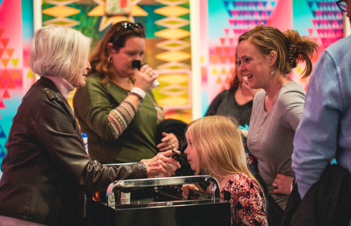 Group of people gathered around a cart smelling and touching art elements.