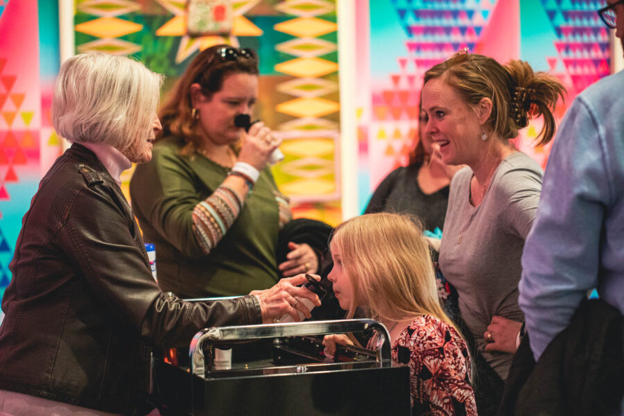 Group of people gathered around a cart smelling and touching art elements.