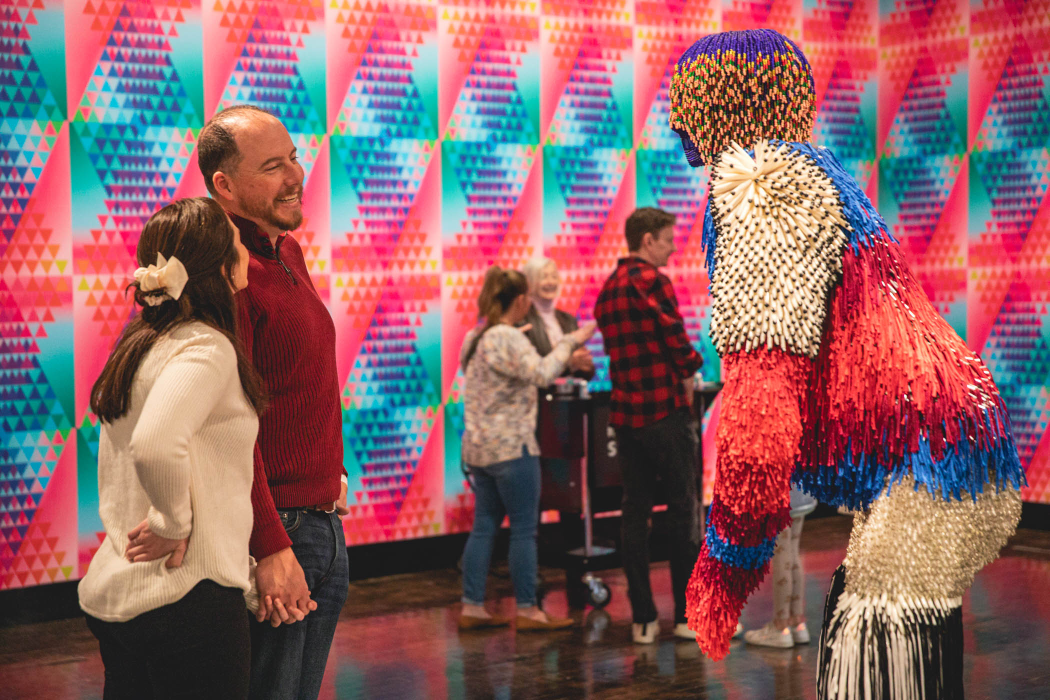 Couple holding hands smiling while looking at the large beaded creature in the gallery
