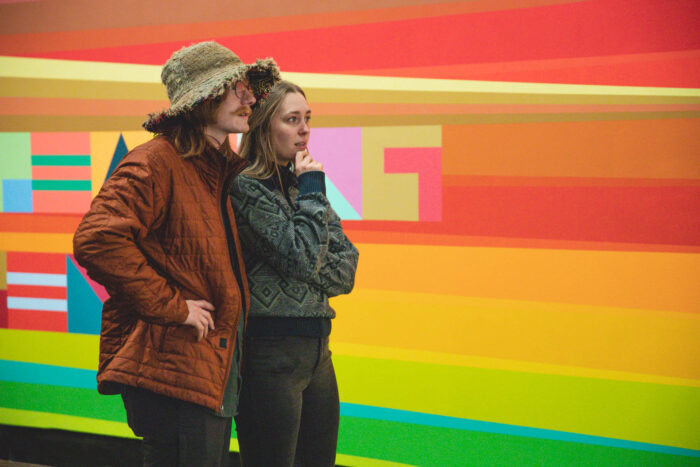 Couple viewing exhibition with multi-colorful striped mural behind them