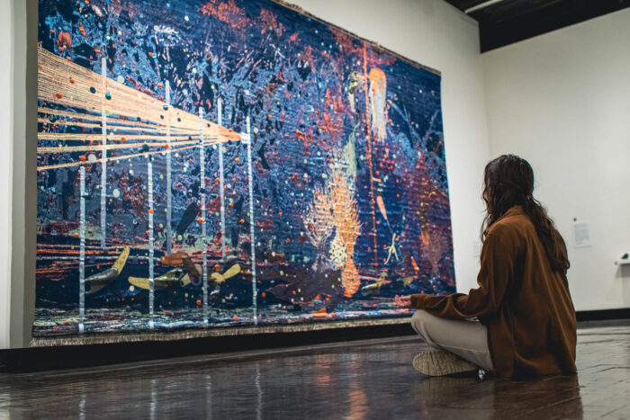 Woman meditating in front of a large, colorful tapestry