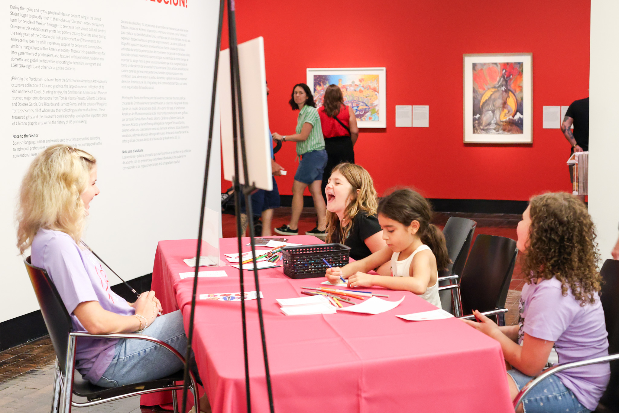 Kids and a Frist volunteer drawing at a table in an art gallery space.