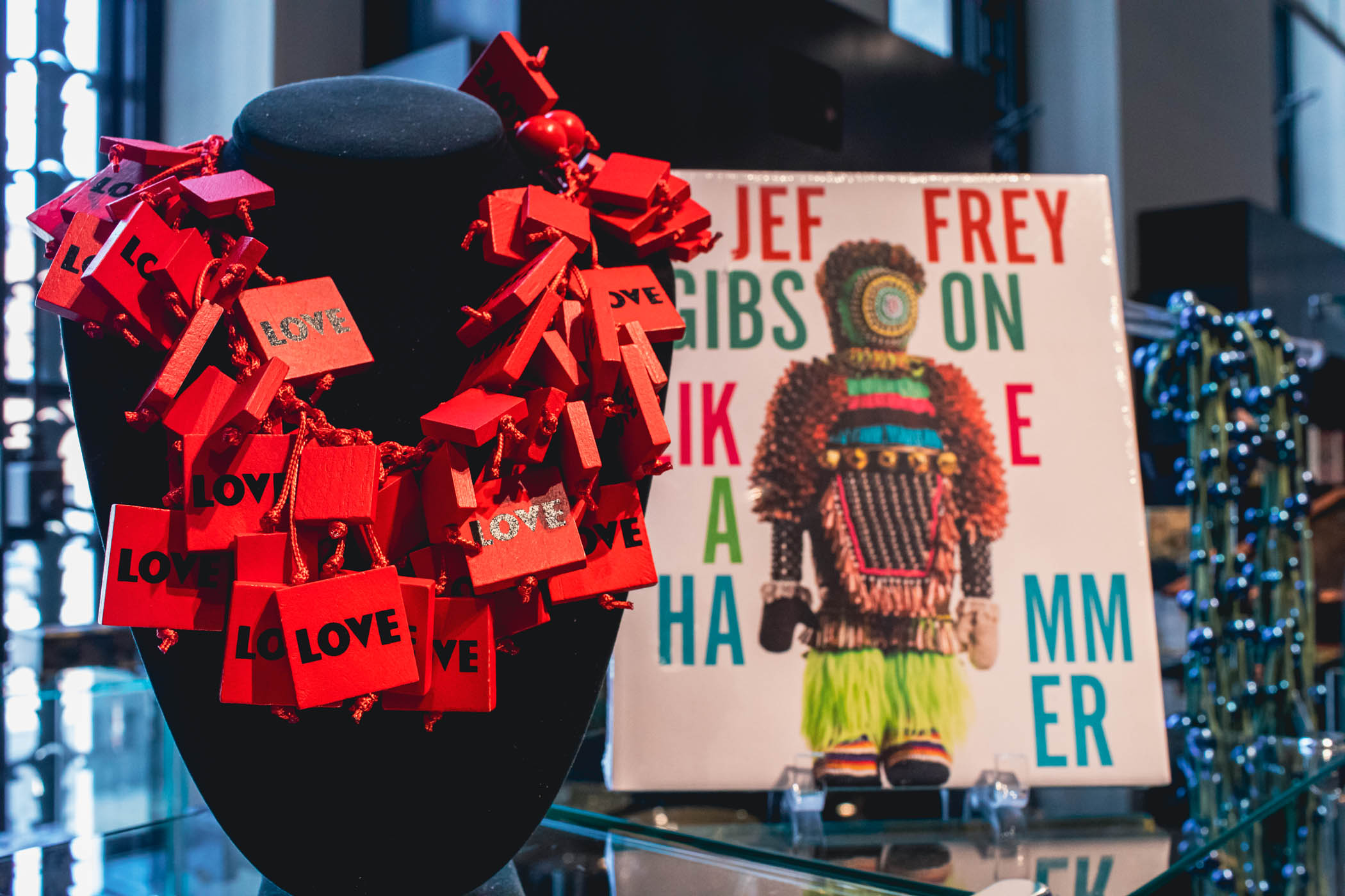 Black felt mannequin with necklace of red blocks next to an art book