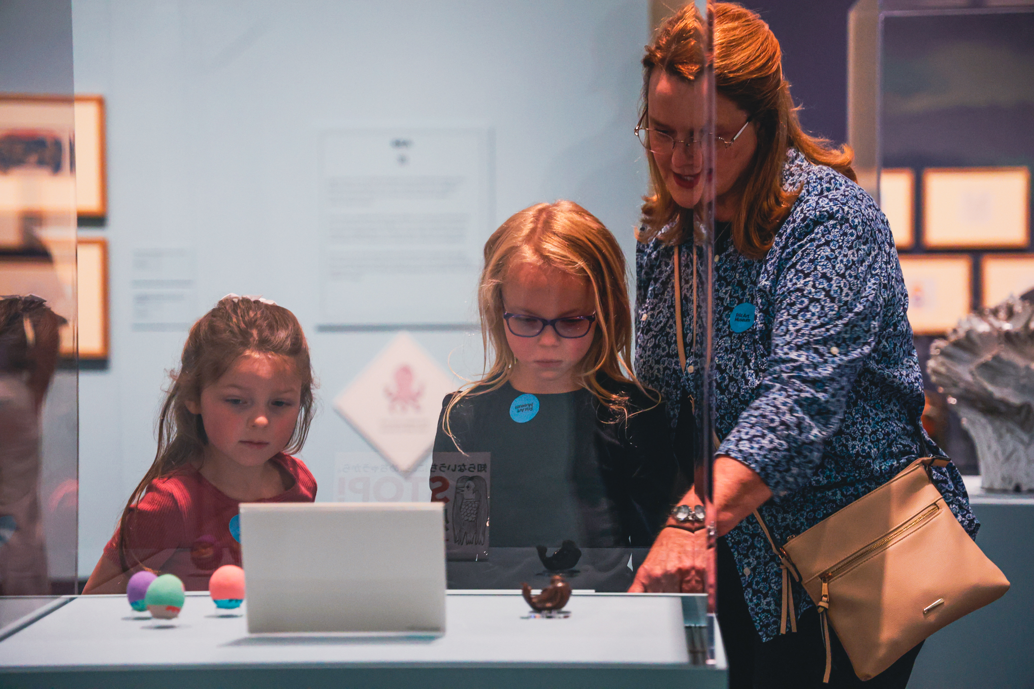 A woman is showing an artwork to two children in the gallery