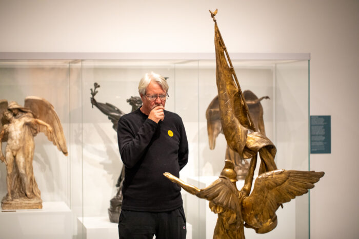 Older man looking at a gold sculpture with his hand cupped around his chin