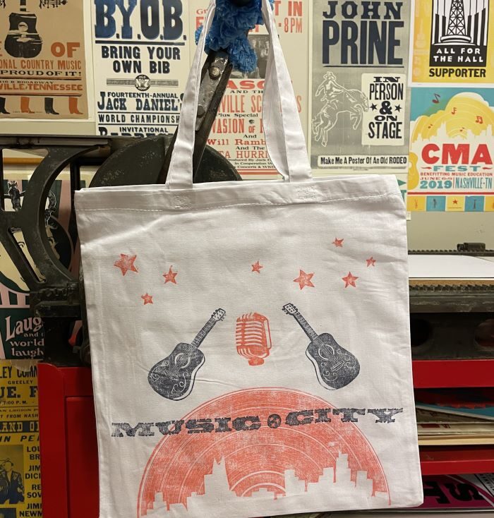 Offwhite tote with prints of guitars and the Nashville City skyline on a record shape with Music City type written above it.