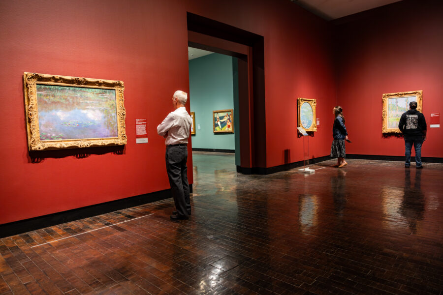 Guests looking at impressionist paintings in a gallery with red walls.