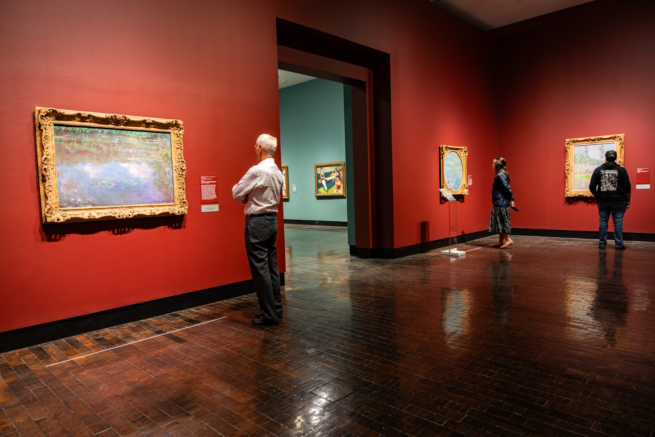 Guests looking at impressionist paintings in a gallery with red walls.