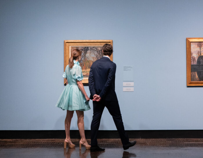 A man and woman look at a painting together in a museum.