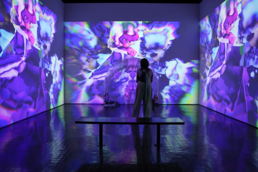 Woman standing in a room filled with abstract purple and pink shapes projected on the walls