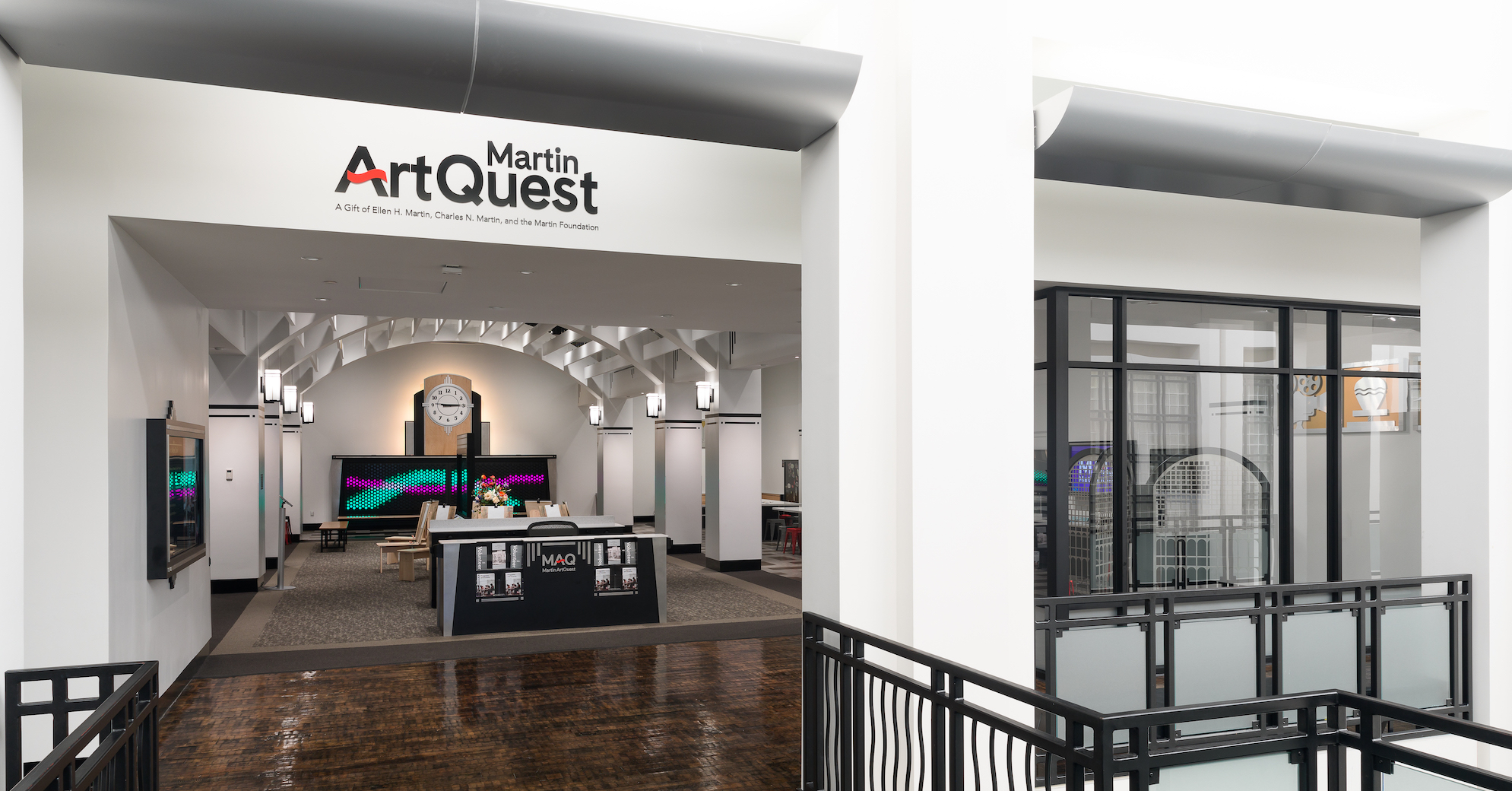 The entrance to Martin ArtQuest before opening for the day. The logo is seen above the door. A desk greets patrons at the entry. A large backlit clock is on the back wall. 
