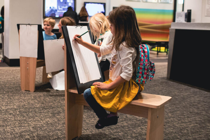 Young girl sitting at an easel drawing. 