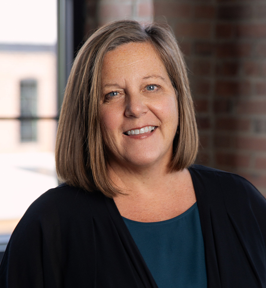 Mary Roskilly smiles in front of a window and brick wall.