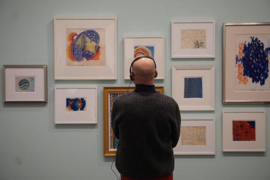 Man with headphones looking at a wall of colorful abstract paintings