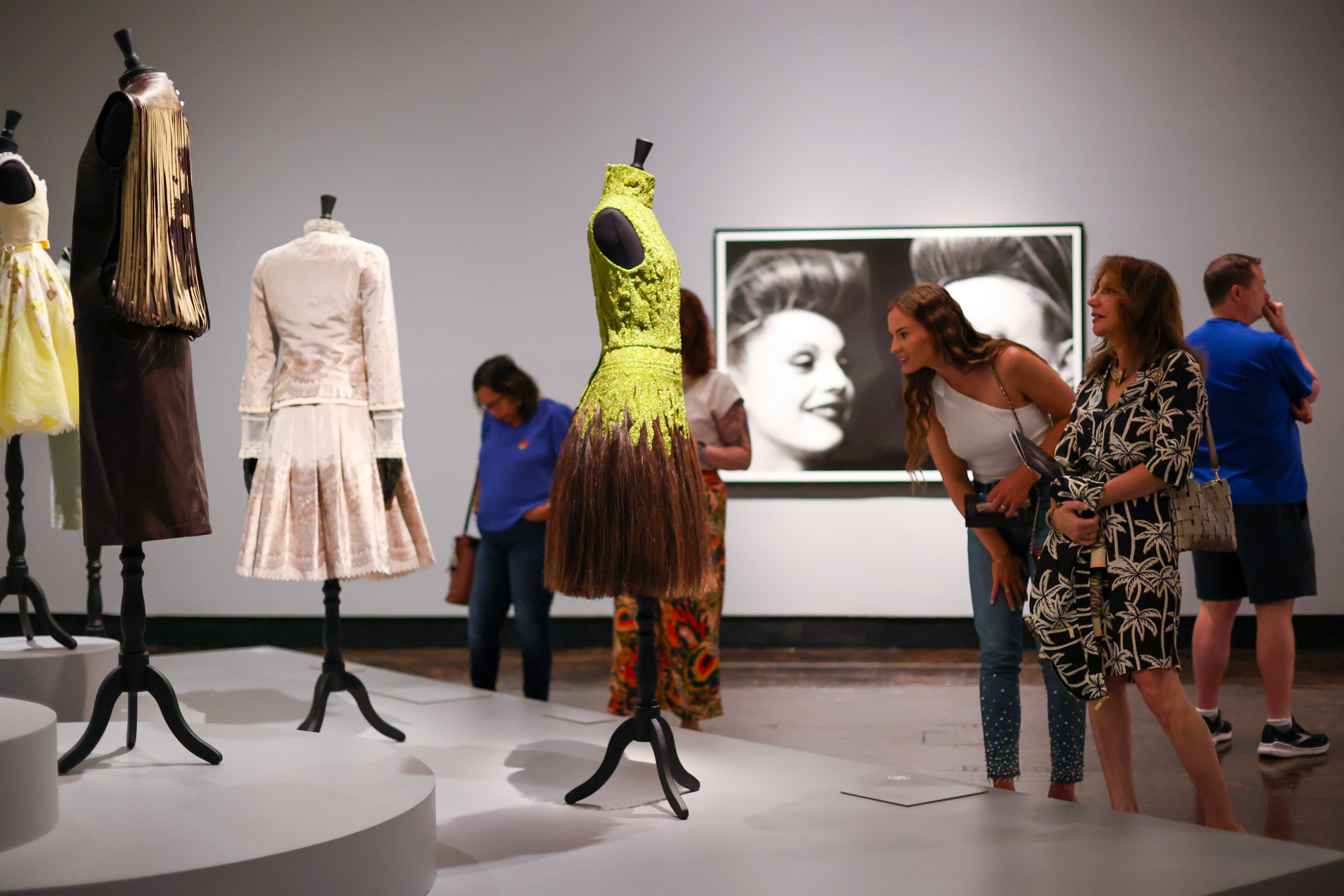 Two women looking closely at dresses on display in a gallery