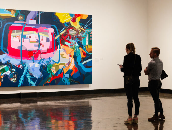 Two people looking at a large vibrantly colored abstract painting