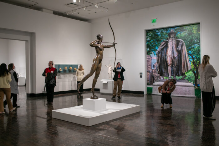 People walking around a large bronze sculpture of Diana shooting a an arrow