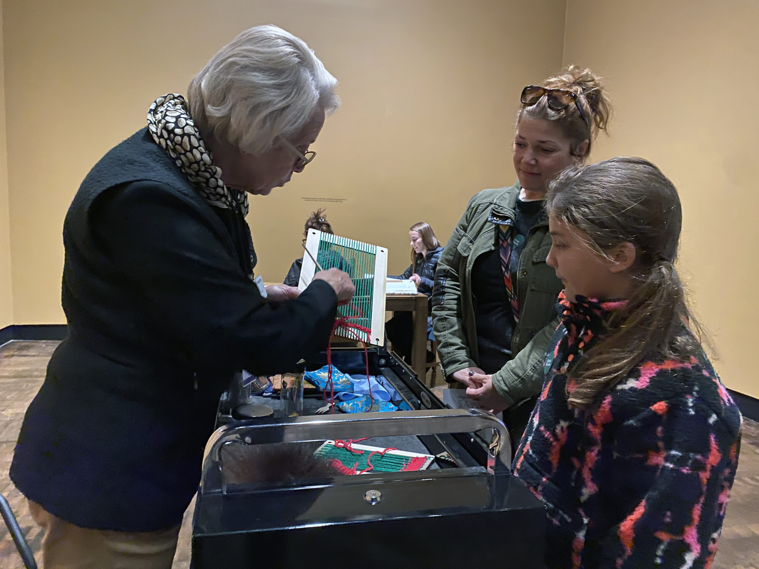 Volunteer showing a mother and daughter a weaving activity in the gallery