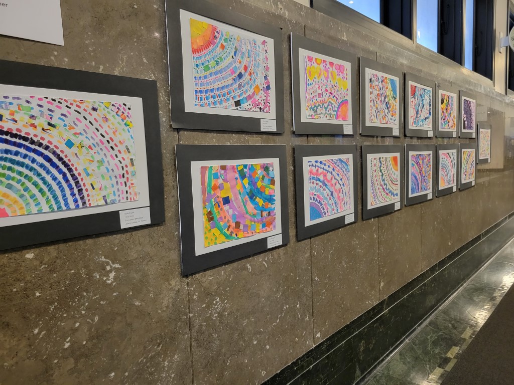A wall is filled with colorful artwork made by students