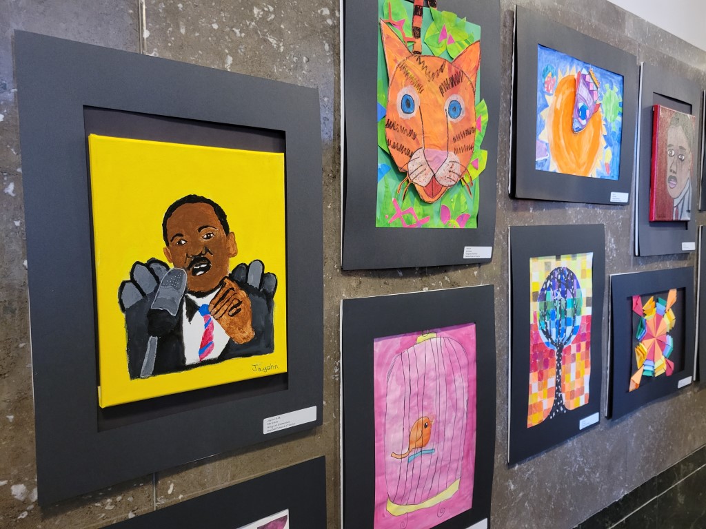 A wall is filled with colorful artwork made by students