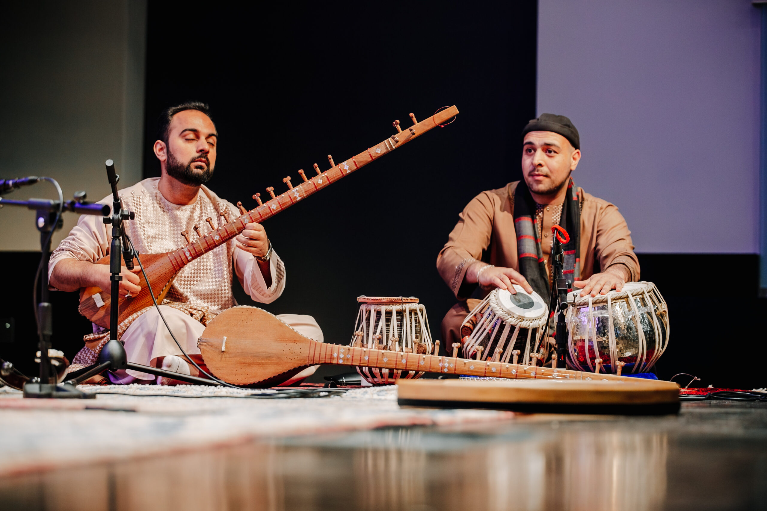 Two men sitting on the floor playing instruments.