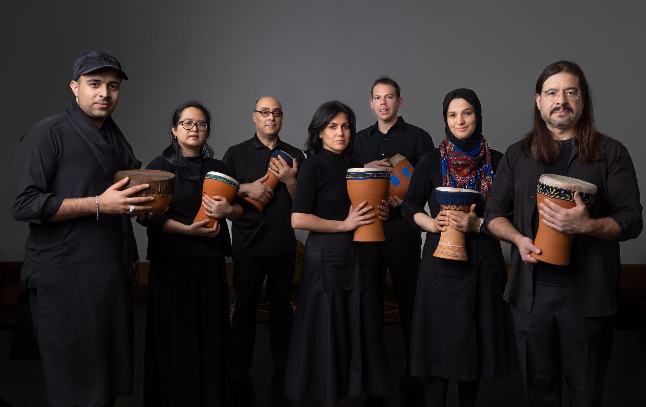 A group of musicians all dressed in black pose with hand drums