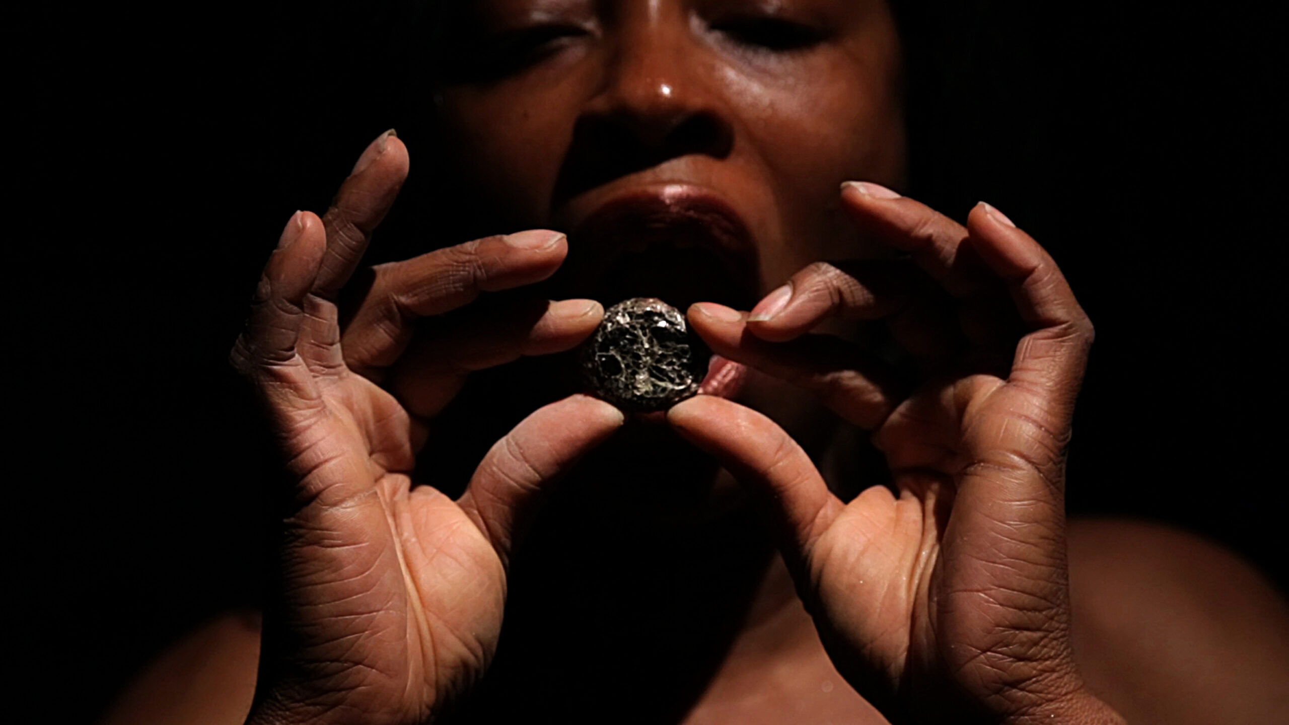 African american woman holding up a shiny stone in her hands in front of our open mouth.