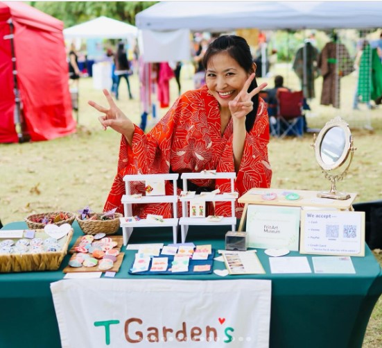 Nozomi Takasu smiling and working a booth with her merchandise