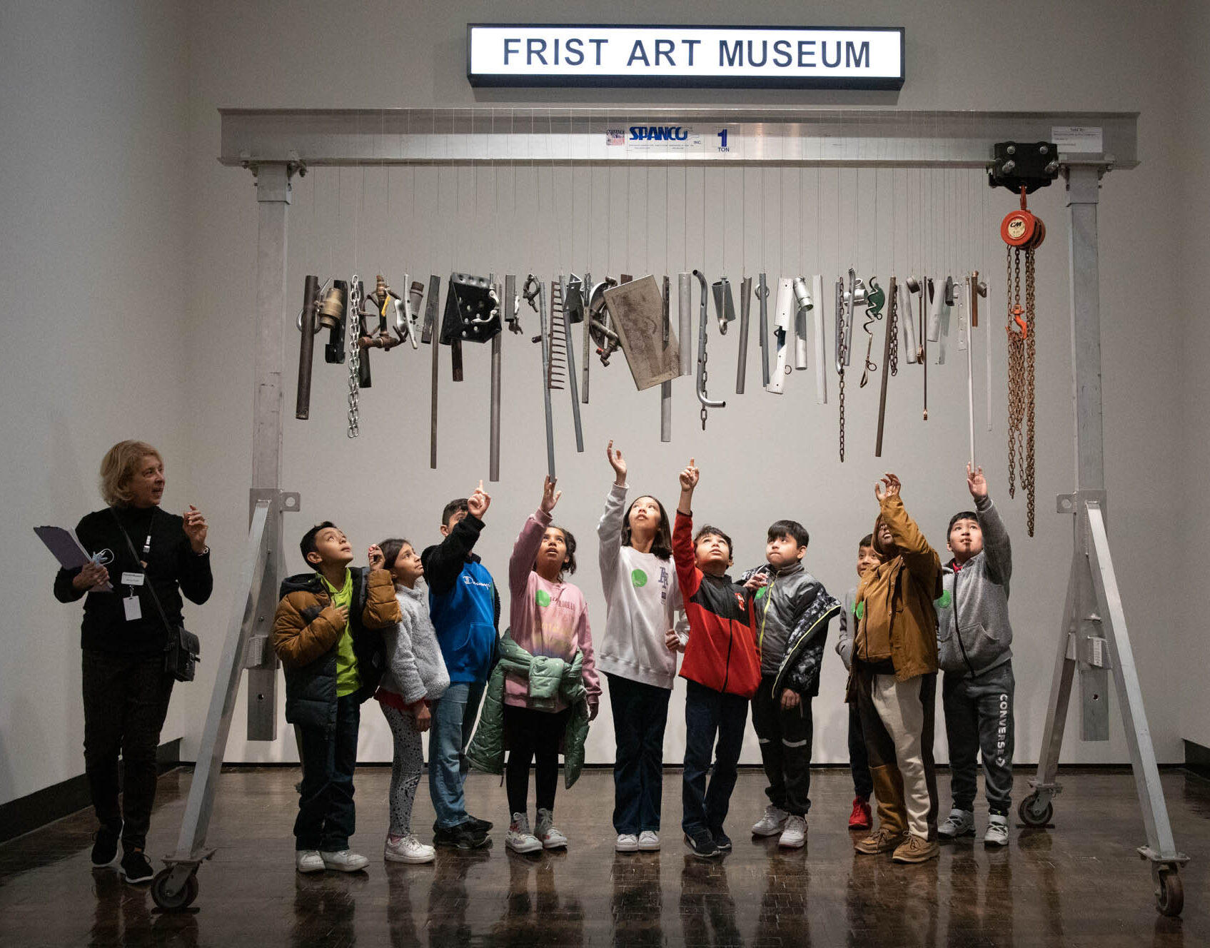 Line of children reaching up to touch a chime made of found objects