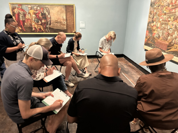 A group of people write in an art gallery.