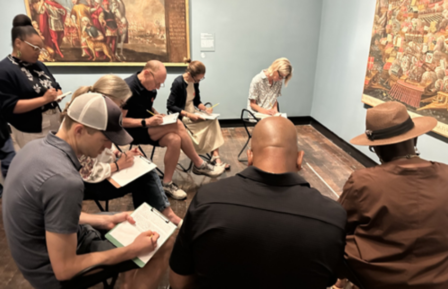 A group of people write in an art gallery.