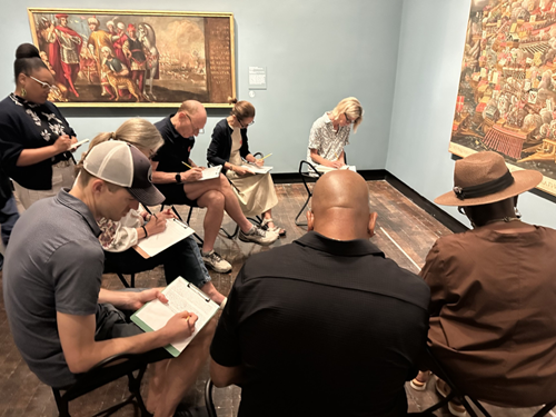 A group of people write in an art gallery.