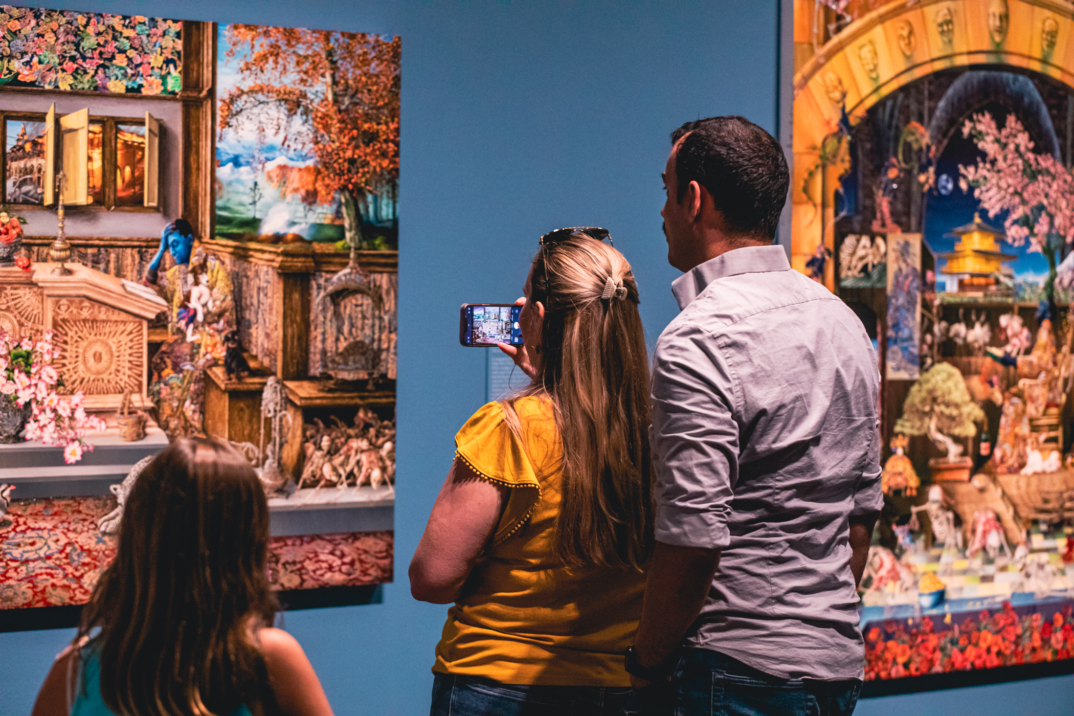 Couple and small child looking closely at and taking a photo of Raqib Shaw's artwork.
