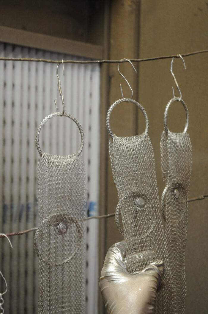 The artists hands inspect pieces of metal mesh to be used in her jewelry.