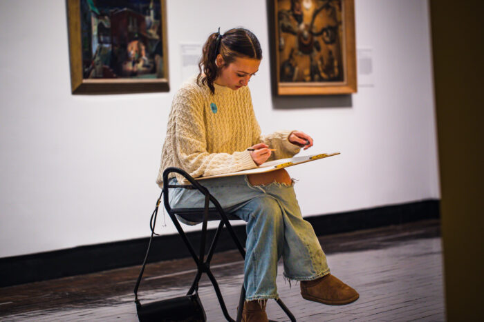 Young woman sitting on a stool drawing on a lap easel
