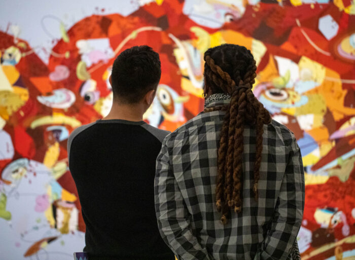The backside of two men facing a colorful abstract painting