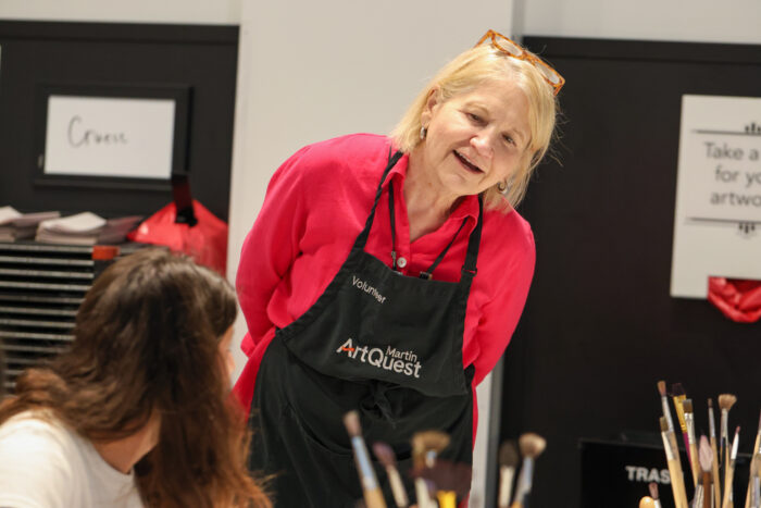 Woman wearing a red shirt with a smock reading "volunteer" and  "Martin ArtQuest"