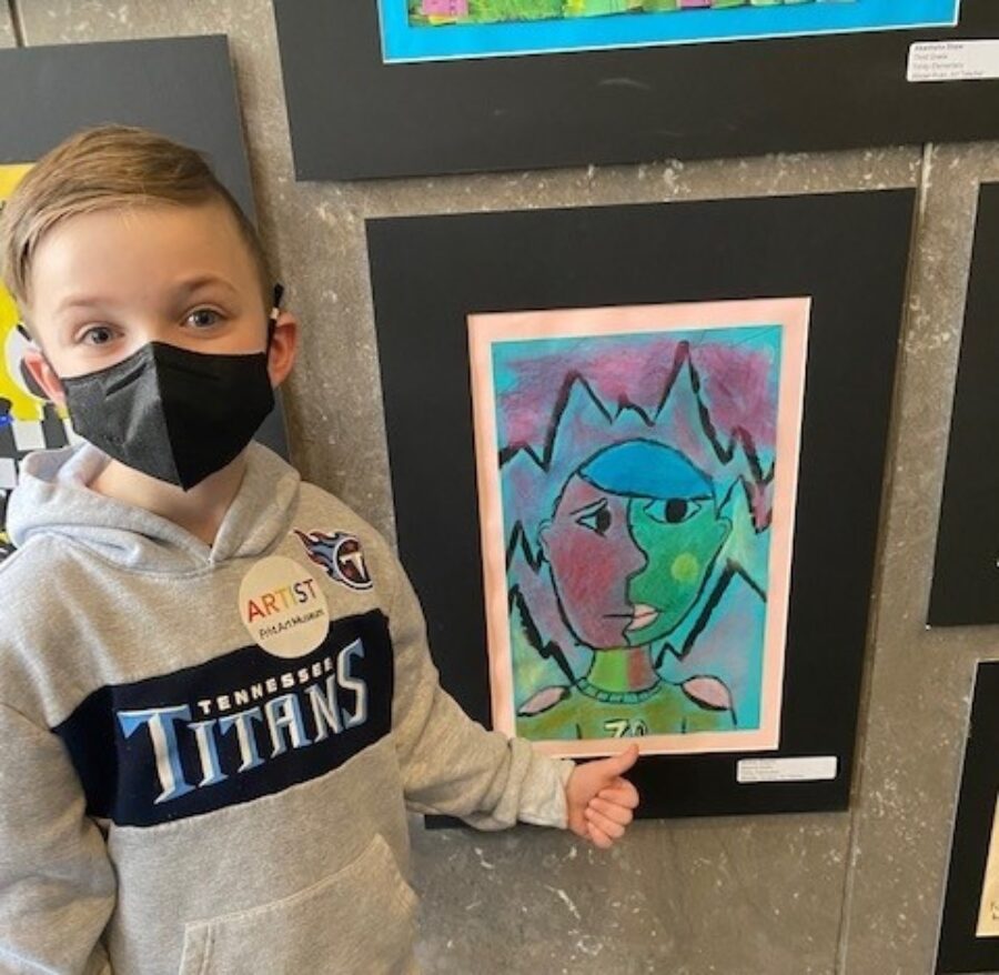 Young boy with a mask on points to his work of art