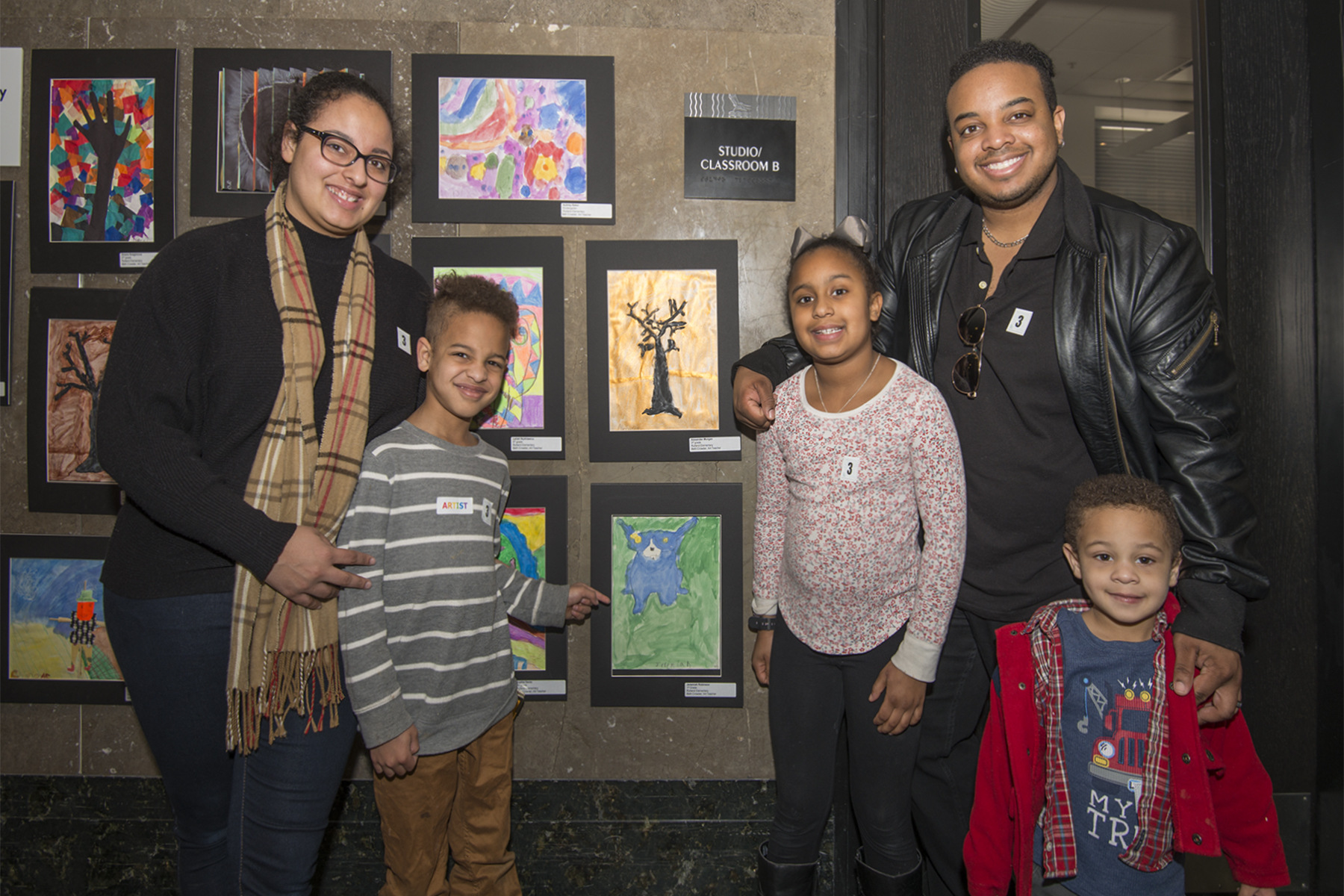 A proud young artist, standing with his parents, brother and sister, points to his blue dog painting on display at the Mayor’s Art Show at the museum.