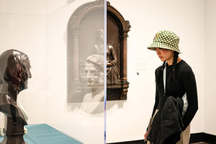 Young woman with hat looking at a bust