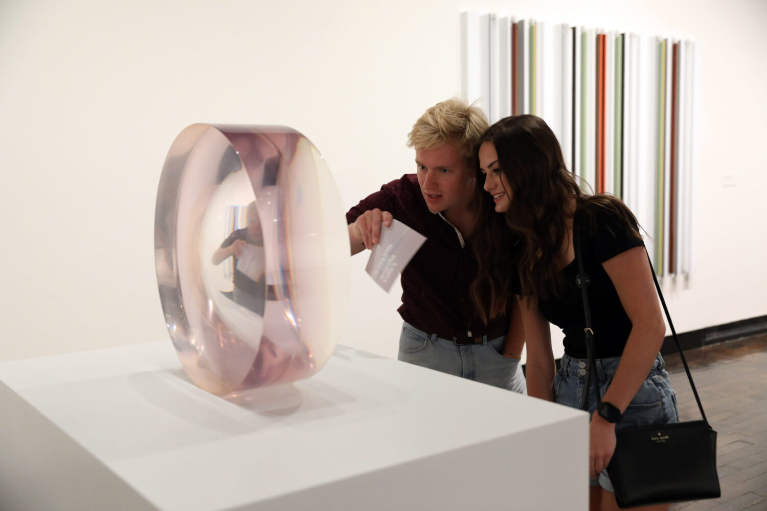 Young couple looking closely at a round pink reflective work of art