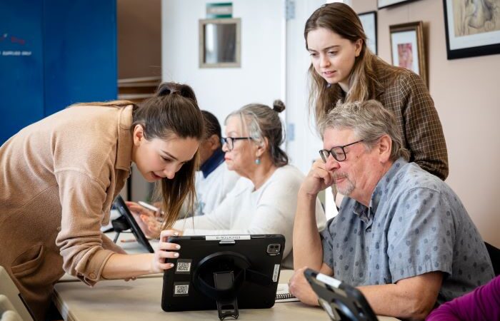 Woman leaning down to look at an iPad as a man looks on.