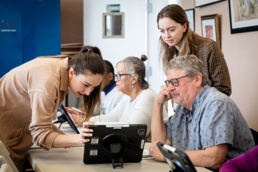 Woman leaning down to look at an iPad as a man looks on.