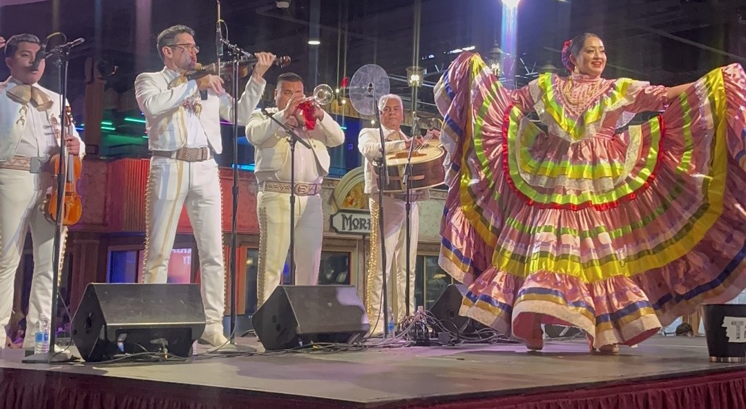 Mariachi band playing on stage with a dancer in a long colorful dress