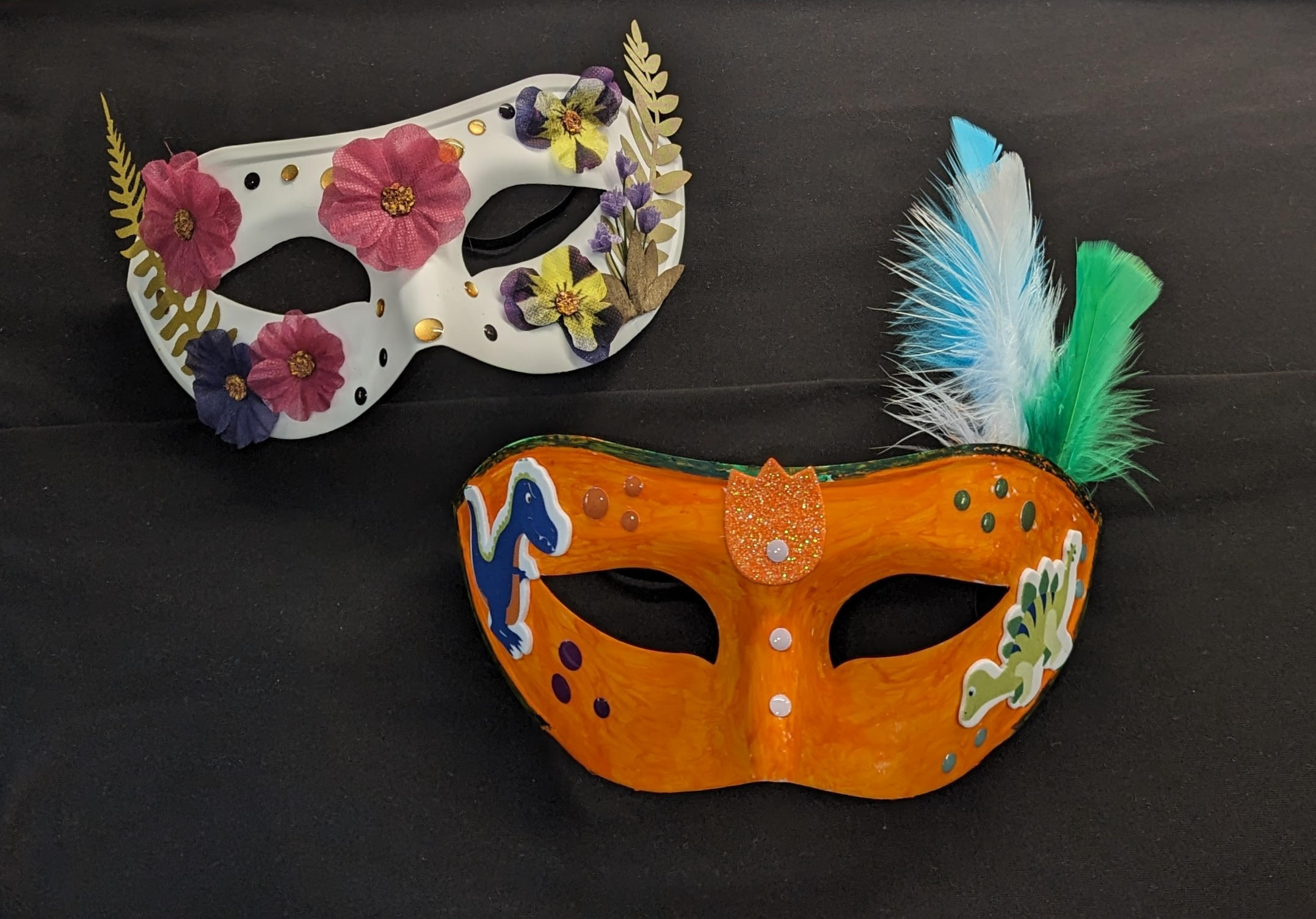Two colorful paper masks adorned with feathers, stickers and jewels.