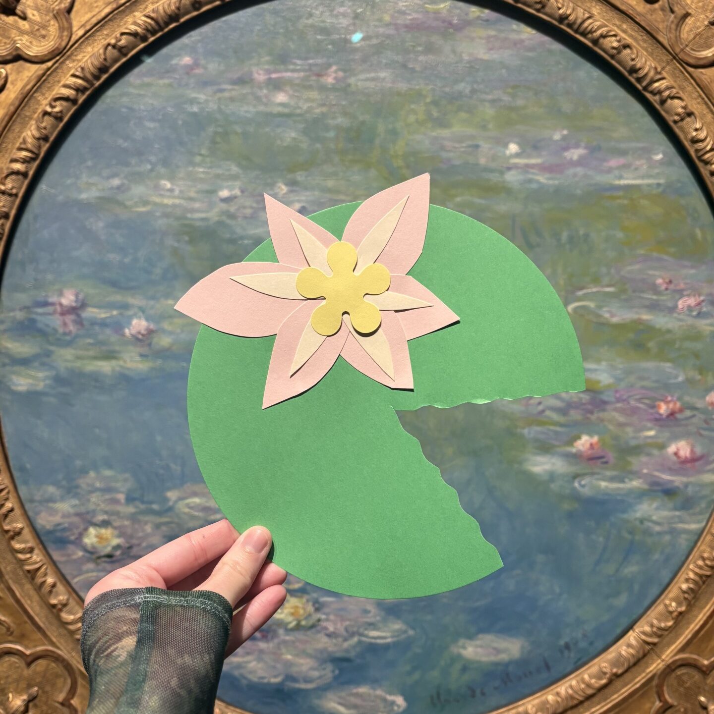 A paper lily pad held in front of a Monet painting of water lilies. 