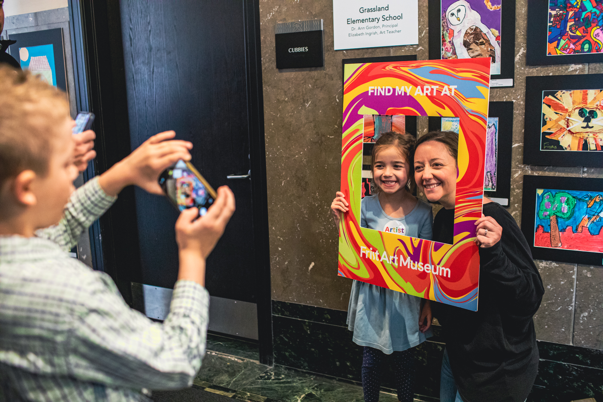Young students stands with her teacher with a colorful paper frame around their faces that says 