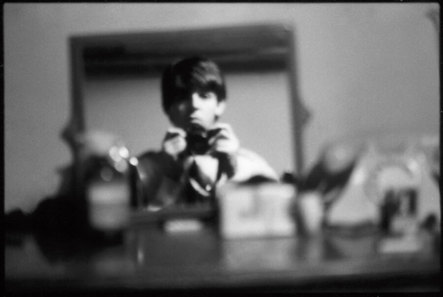 A young Paul McCartney holding a camera taking a photo of himself in a mirror